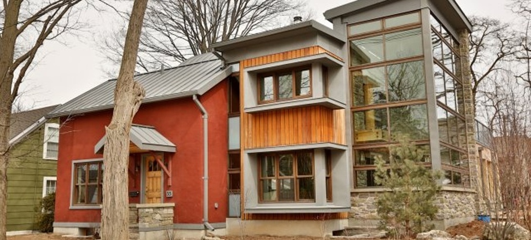 Modernt bostadshus med hållbara fasadmaterial som träpanel, metalltak, stenbas och energieffektiva fönster.
