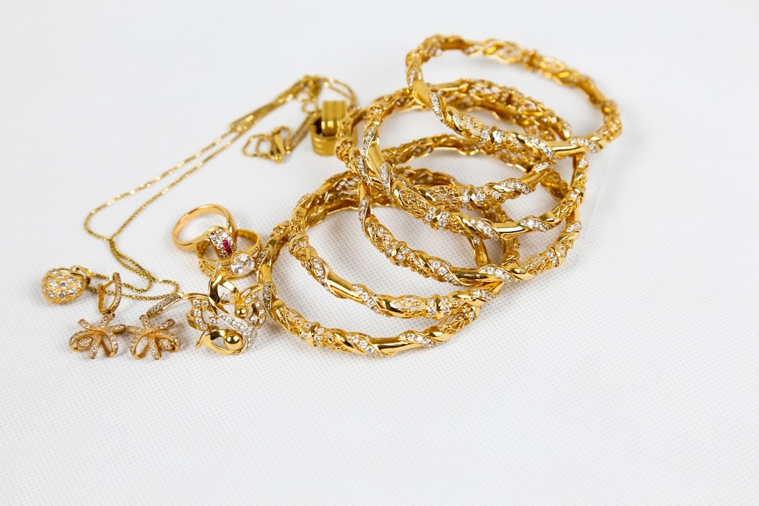 En elegant samling guldsmycken med utsmyckade armband, ringar med ädelstenar och delikata halsband på en vit yta.