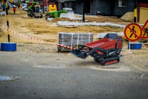 En röd minidumper på en byggarbetsplats med avspärrningar och andra maskiner i bakgrunden.