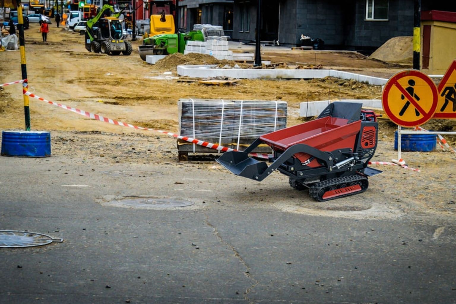 En röd minidumper på en byggarbetsplats med avspärrningar och andra maskiner i bakgrunden.